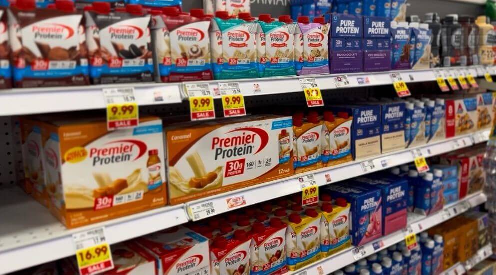 A supermarket aisle shelf filled with various protein drinks, prominently featuring Premier Protein and Pure Protein brands