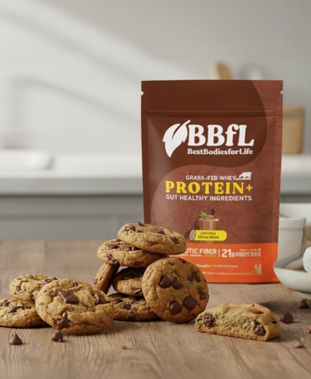 A bag of BBFL grass-fed whey protein powder stands behind a stack of chocolate chip cookies.