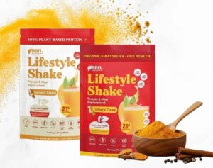 Two packages of BBFL Lifestyle Shake turmeric cream protein powder stand next to a bowl of turmeric powder.