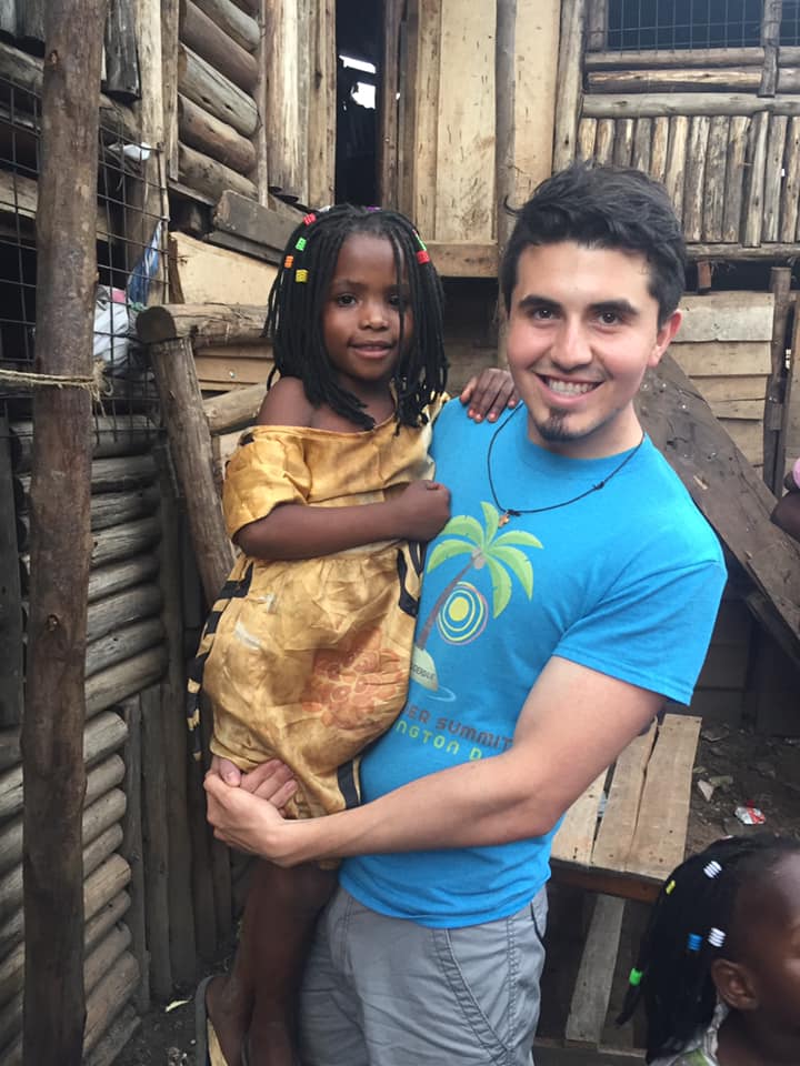 Raul, a man in a blue t-shirt, smiles as he holds a young girl dressed in an earth-toned outfit