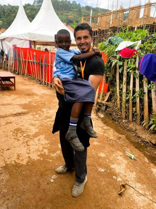 Raul smiling, holds a young child in uniform during a community outreach event.