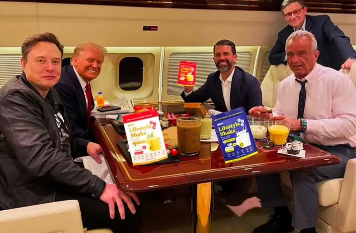 Elon Musk, Donald Trump, Donald Trump Jr., Robert F. Kennedy Jr., and two other men are seated around a table inside a private jet, with various drinks and "Lifestyle Shake" products on display.