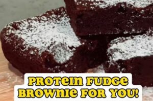 Three dark chocolate brownies, generously dusted with powdered sugar, are shown with the text "PROTEIN FUDGE BROWNIE FOR YOU!" at the bottom.