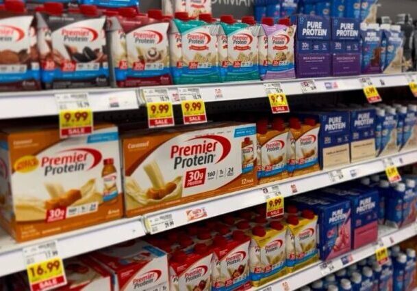 A supermarket aisle shelf filled with various protein drinks, prominently featuring Premier Protein and Pure Protein brands